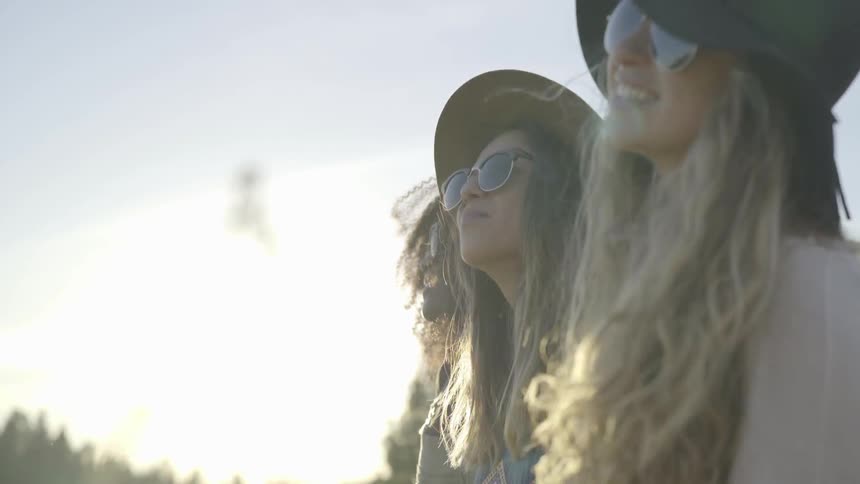 Three woman in sunglasses laugh together in field