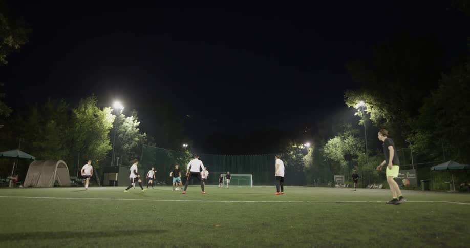 Two teams of men play soccer in a field at night