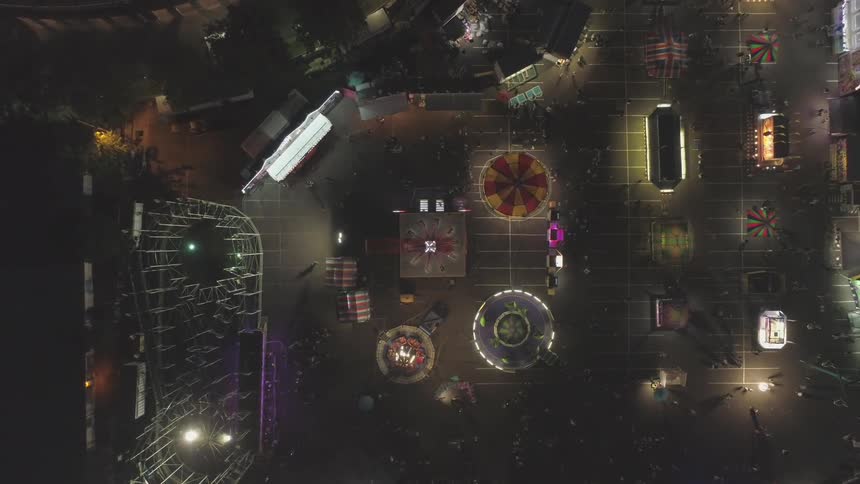 Amusement park seen from an aerial perspective at night time with park lights glowing neon on the rides and stands