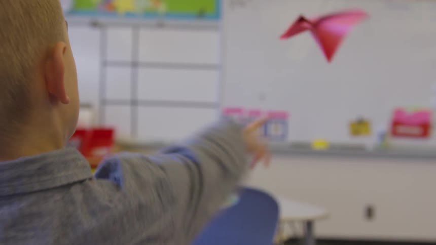 A little boy throws a red paper airplane