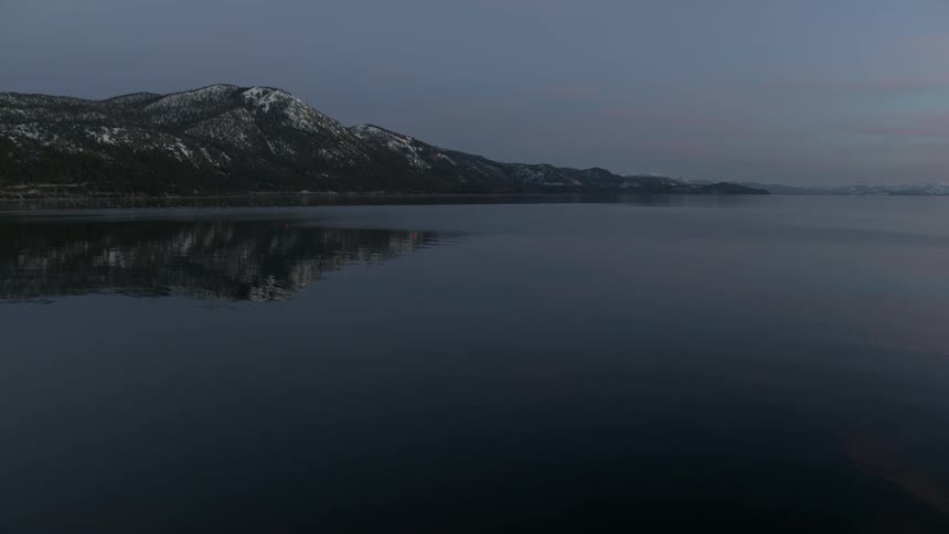 Still water on a nice calm sunset or sunrise day with trees and snow capped white mountains