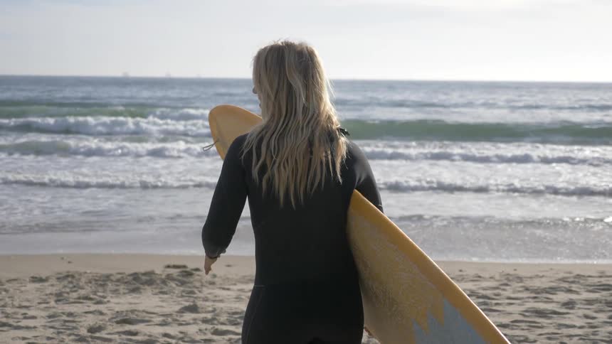 Woman with surfboard looks at ocean