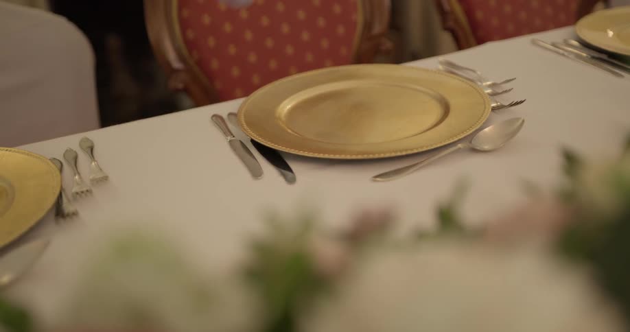 A gloved person placing cutlery next to gold plates