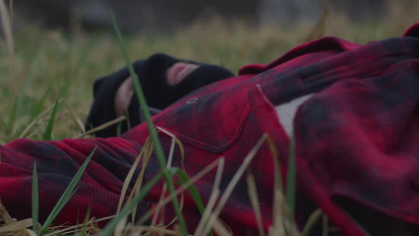 A man is lying asleep on the grass wearing a ski mask