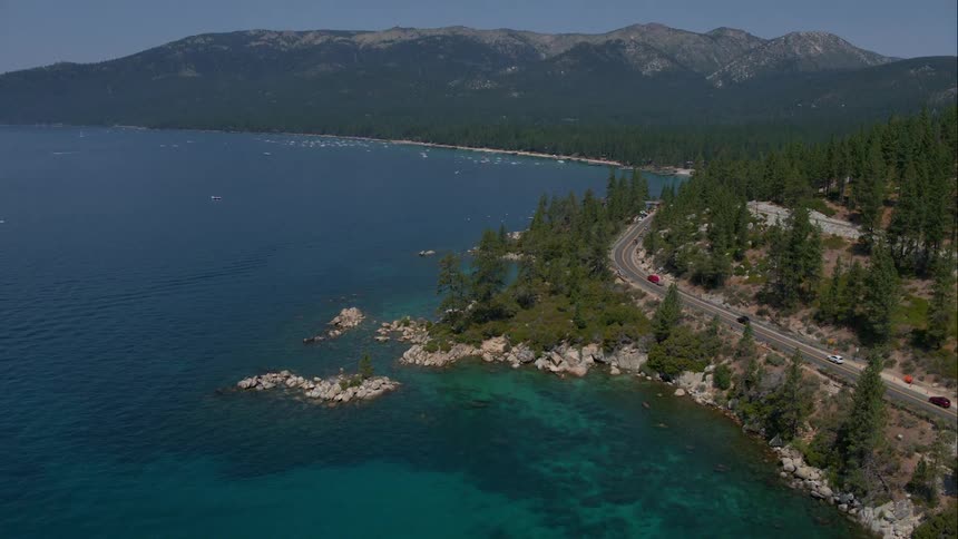 Bright blue water surrounded by rocks trees mountains and a small roadway