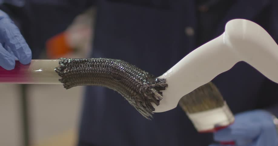 Employee uses a brush to cover a handlebar with lacquer inside a warehouse
