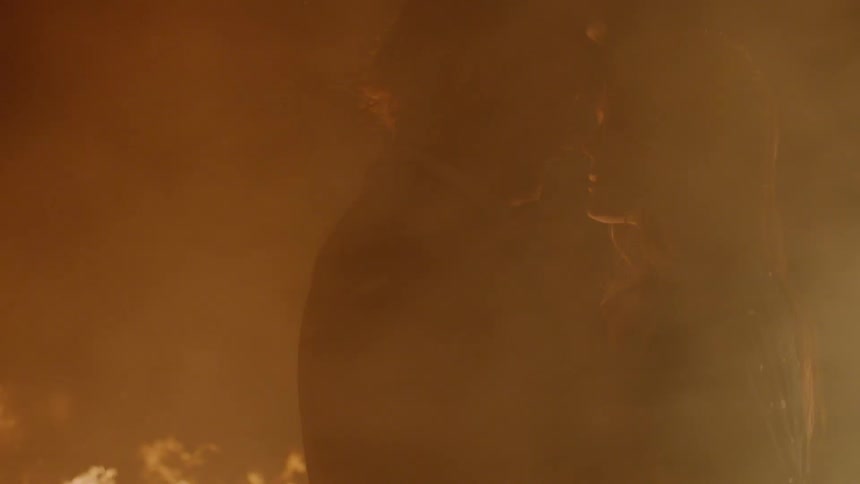 A man and a woman kiss as they are surrounded by smoke standing in front of a fire