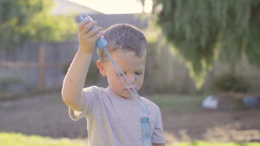 Boy blows bubbles outside a smiles as adult watches