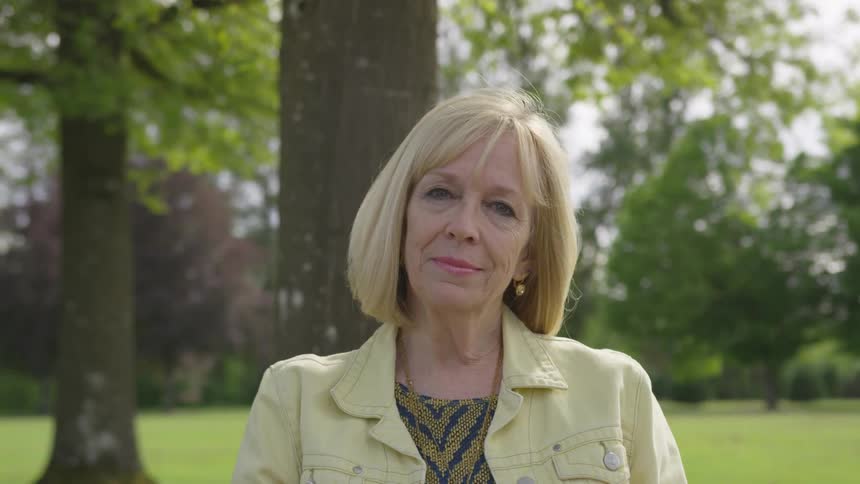 Older woman looks around with trees in the background
