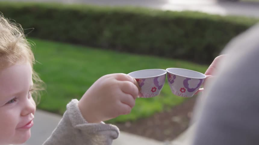 A toddler and adult are having an imaginary tea party with small cups