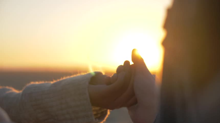 Hand holding in front of sunset