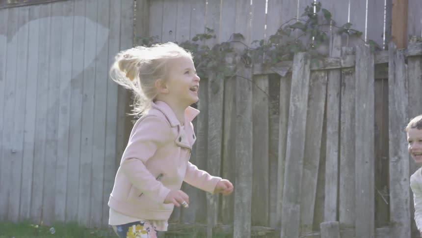 Little boy and girl chasing bubbles in a backyard