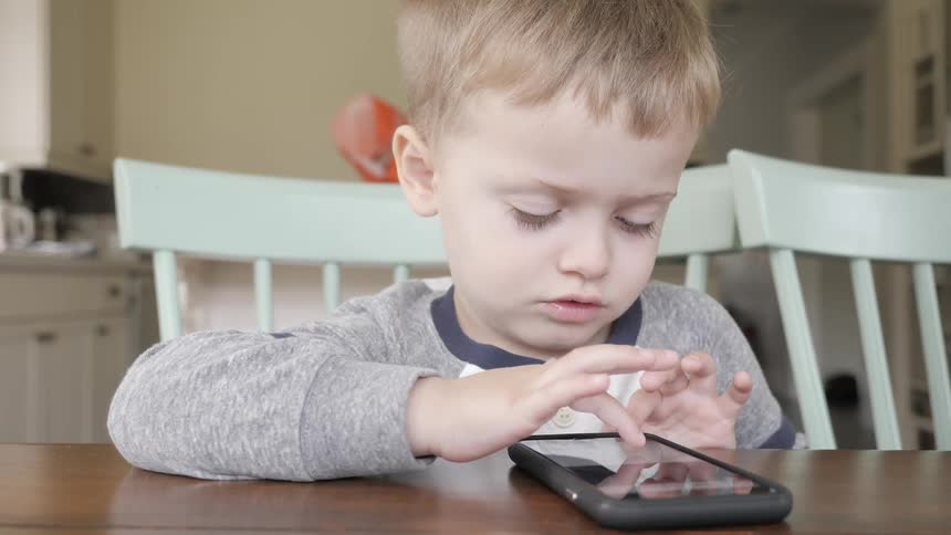 Little boy playing on a cell phone at a kitchen table