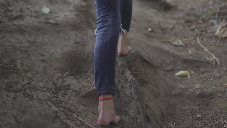 Barefoot woman climbs up a dirt path to the road