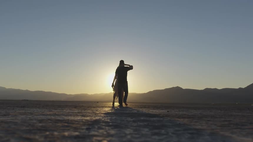 Two people dance in front of a setting sun