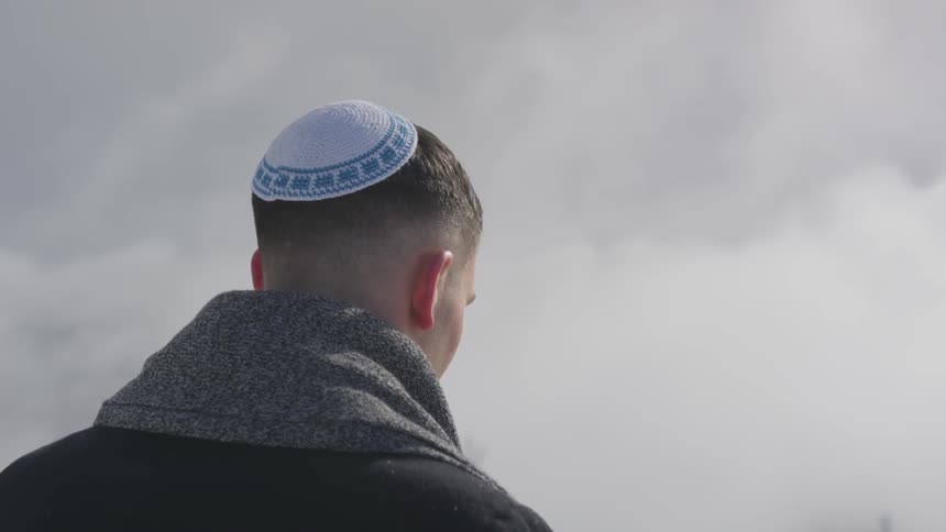Man in yarmulke stands under dark clouds