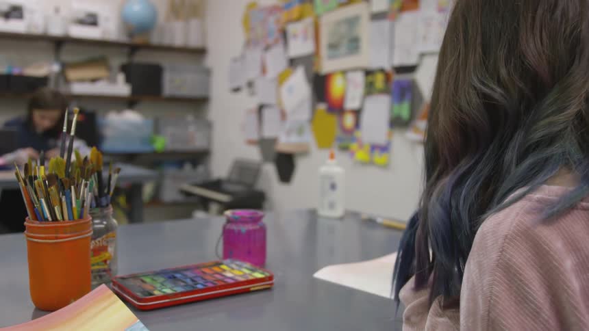 Woman sits at table with art supplies