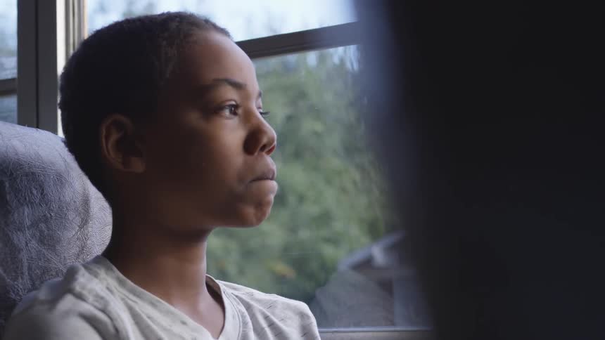 A boy sits next to a window while riding a bus