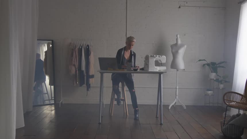 Woman is sitting at desk with laptop and sewing machine