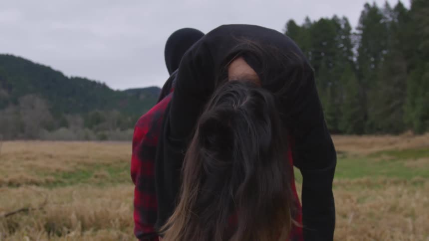 A man carries a woman over his shoulder through a field