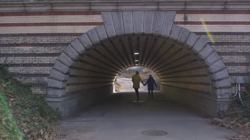 Two people hold hands walking through a tunnel