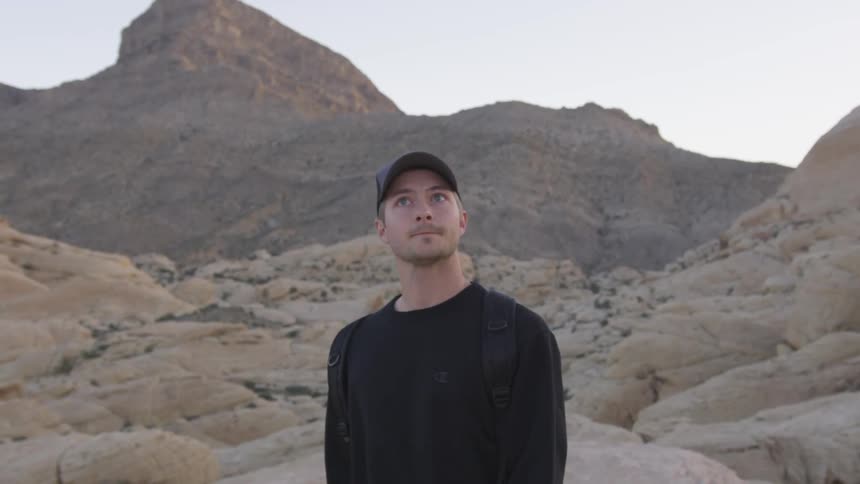 A man hikes in the desert up rocky terrain as he looks around