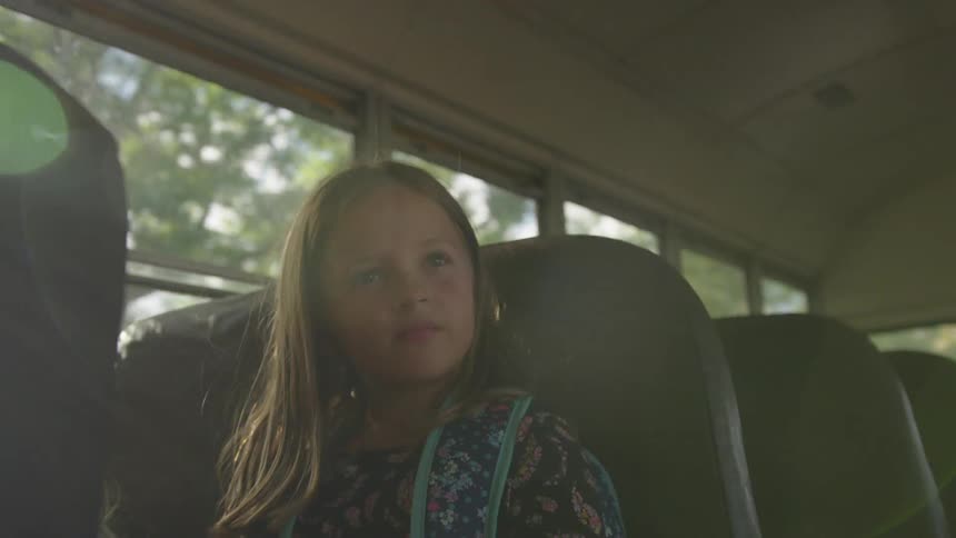 A little girl rides a bus to school as sunlight streams into the bus from behind trees