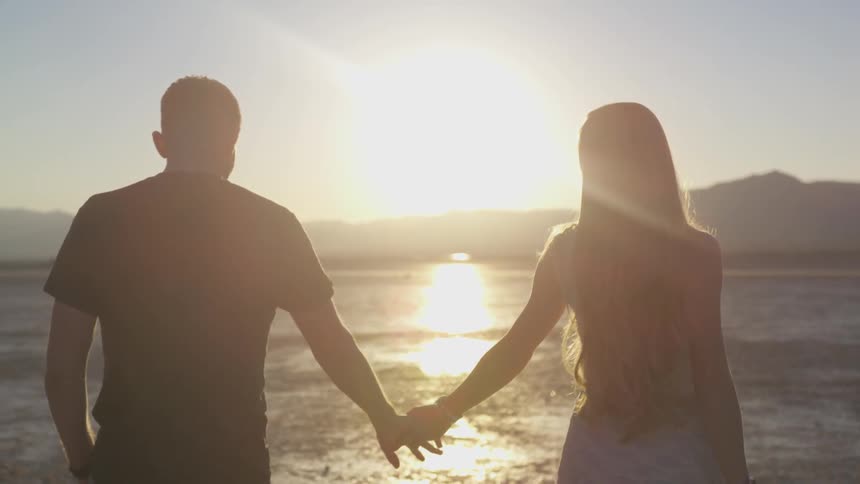 Man and woman holding hands and walking through a dry desert bed during sunrise