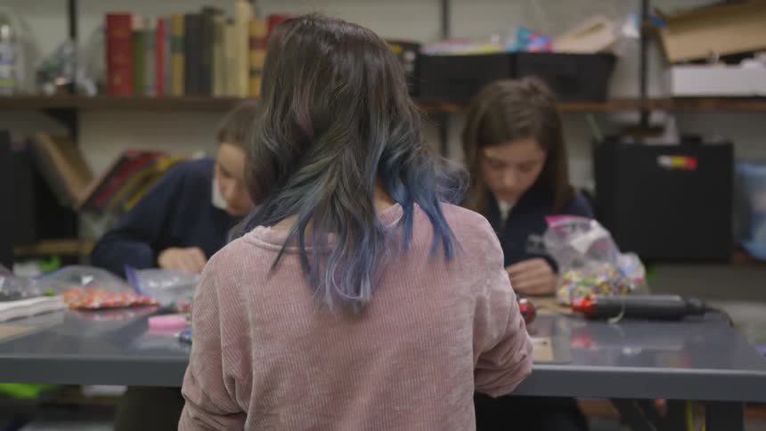 Three woman sit at a table to work on crafts