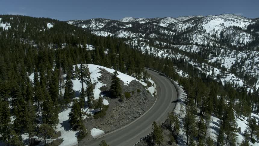 A curved highway in the mountains is surrounded by a forest