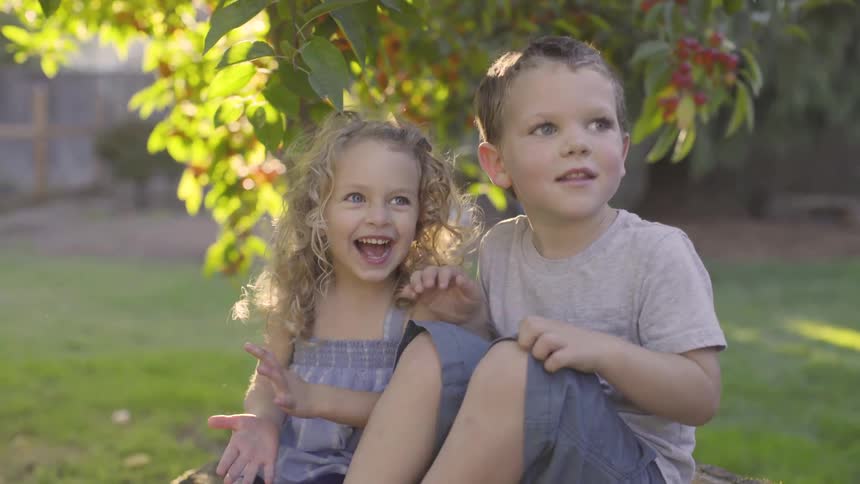 Boy and girl smile sitting under tree in bright sunshine