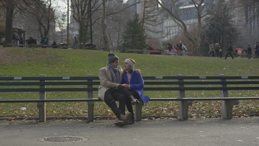 Two people sit together on a long park bench