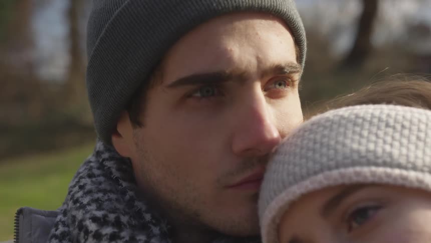 A woman leans against a man while he looks into the distance