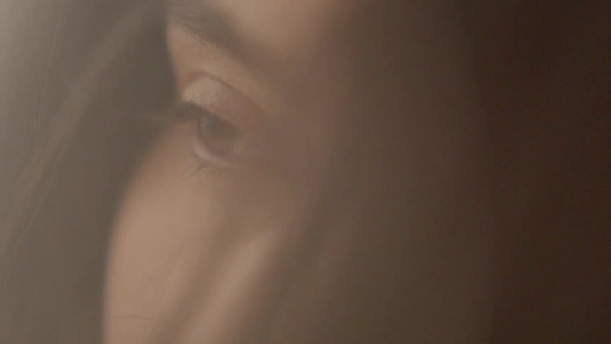 A woman slowing opening her eyes with her hair blowing