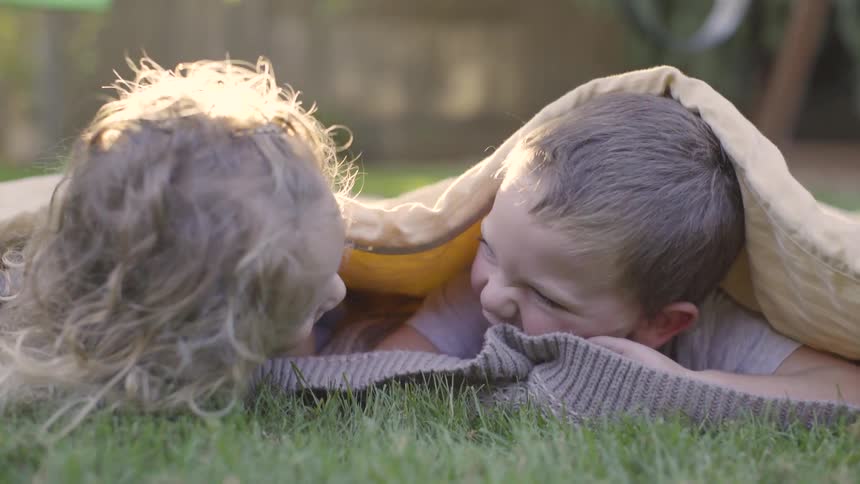Children laugh together as they sit on the grass under a blanket