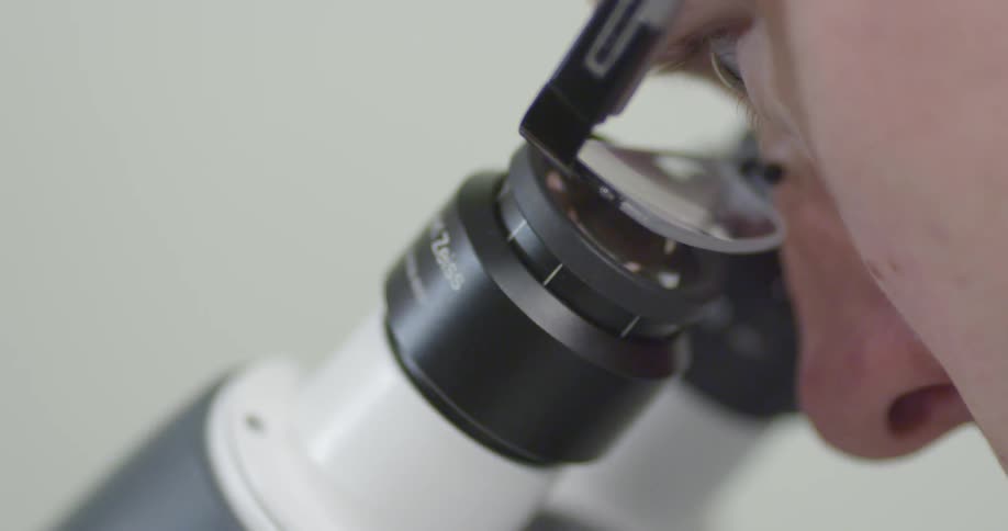 Person looking through lens of microscope