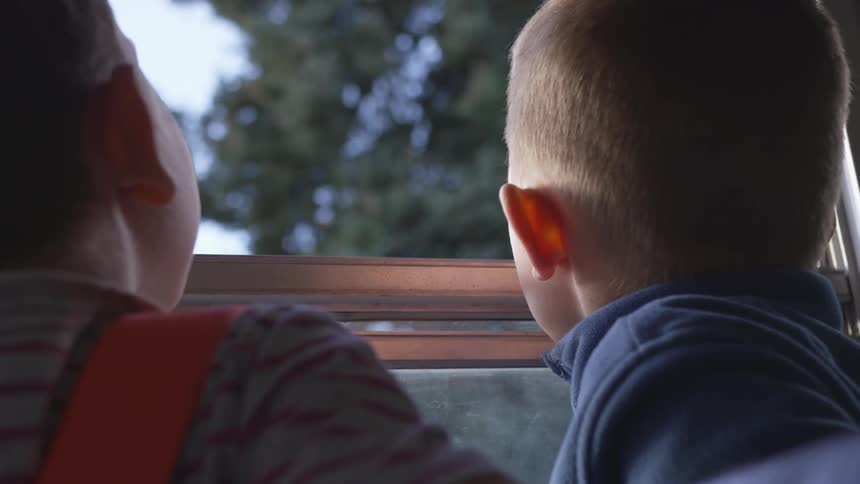 Back of heads of two boys looking out the school bus window as it drives on a sunny day