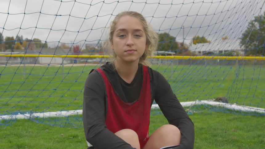 A girl sitting in the goal on a soccer field