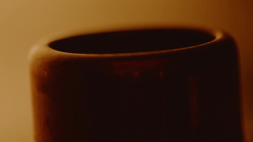 A circle shaped brown lit black object has blurry objects pass in front in a dim lit room
