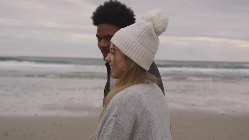 A man and woman laugh while walking on the beach