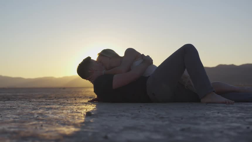 Couple laying in a sunny dirty field kissing