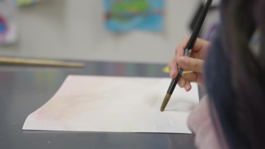 A little girl uses watercolor paint on a sheet of paper