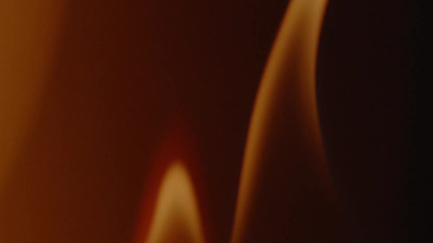 A dense heavy flame flickers with another flame behind it so two flames in a dim lit room