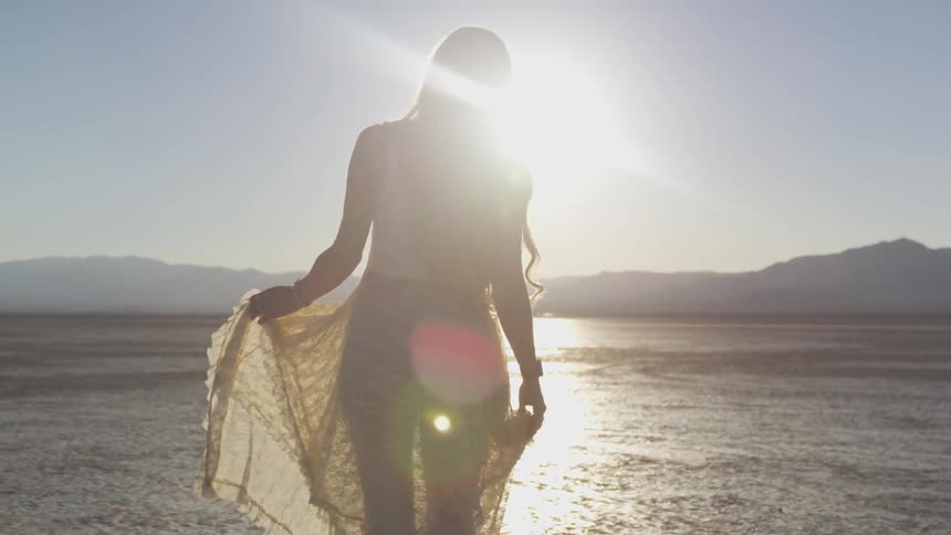 A woman in a lace dress strolls in a desert on a sunny day
