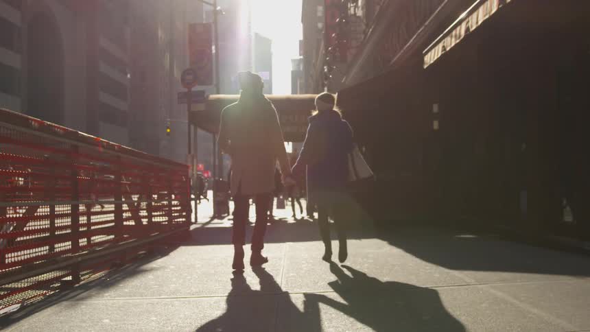 A couple walks down a city sidewalk holding hands