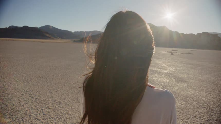 A woman wearing a white dress walking on dry dirt in the sun