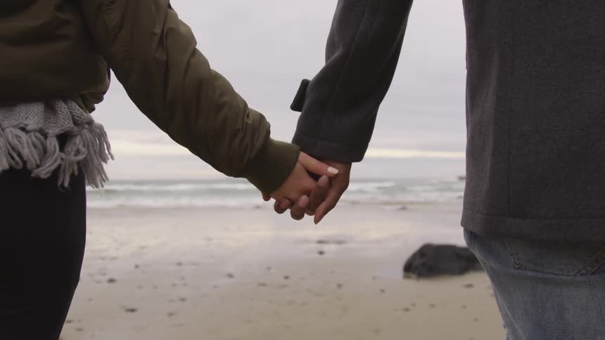 Two people holding hands at the beach on a cloudy day