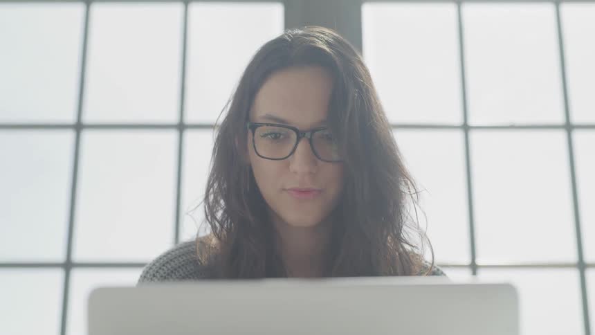 Woman wearing glasses staring at a monitor in a bright room