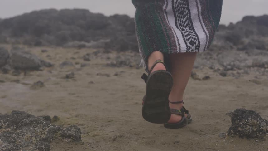 A person hikes over dirt and rocks while wrapped in a blanket