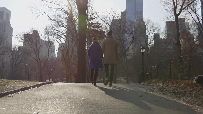 Man and woman walking through a city park while holding hands